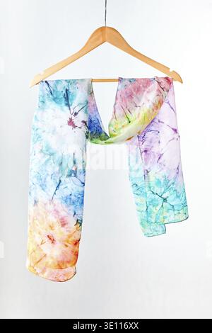 Silk colourful hand painted tied scarf hung on hanger over grey background. Woman fashion, tying a scarf, wearing a scarves. Stylish ways to tie and w Stock Photo