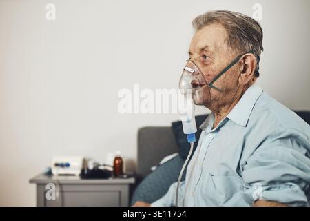 Senior man inhaling airways and lungs applying medicine. Covid-19 or coronavirus treatment. Man breathing through face mask using nebuliser Stock Photo