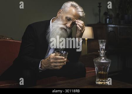 Stylish and handsome bearded senior man drinking whiskey Stock Photo