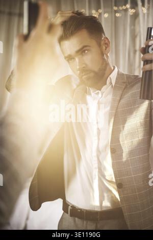 Young and handsome bearded man is using hairspray Stock Photo