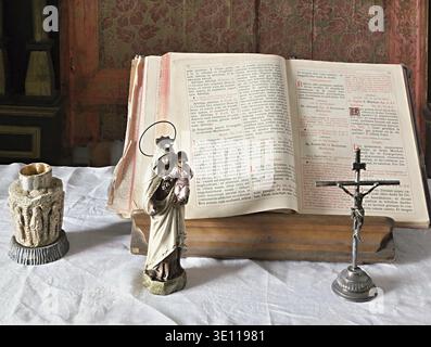 Open bible, crucifix and madonna with child statue resting on white altar cloth in old church Stock Photo