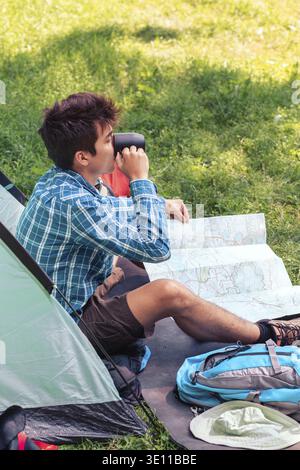 Spending a vacation on camping. Young man planning next trip and drinking a coffee Stock Photo