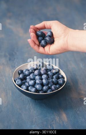 Woman putting freshly gathered blueberries into a small bowl. Table painted in blue in the background Stock Photo
