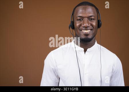 Studio shot of handsome African businessman wearing headset against brown background Stock Photo