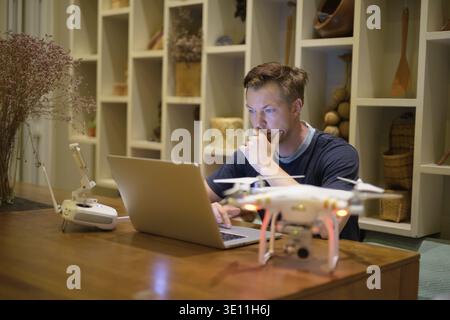 Portrait of young handsome man with drone and laptop in the dining room at home Stock Photo