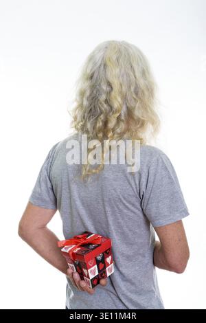 Back view of senior bearded man hiding red gift box behind back ready for Valentine's day Stock Photo