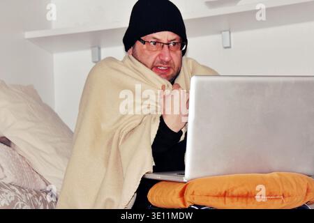 Man sitting on the sofa using computer laptop at home feeling unwell and coughing as symptom for cold or bronchitis. health care concept. Stock Photo