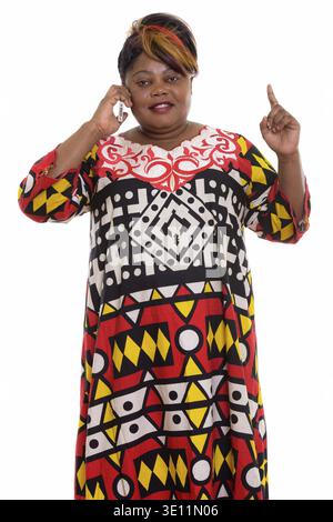 Studio shot of happy fat black African woman smiling while talking on mobile phone and pointing finger up Stock Photo