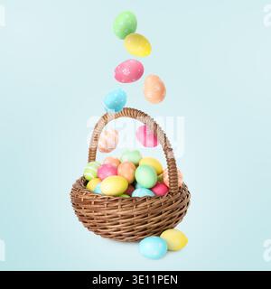 Color Easter eggs falling into basket on light blue gradient background Stock Photo