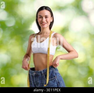 Happy woman in her old jeans against blurred green background. Weight loss result Stock Photo