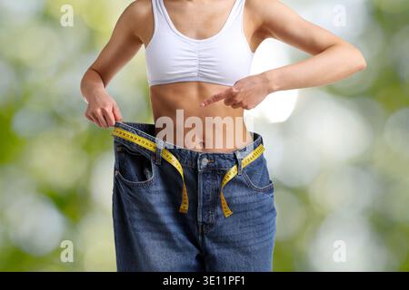 Woman pointing at her old jeans against blurred green background, closeup. Weight loss result Stock Photo
