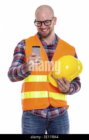 Happy bald muscular man construction worker smiling while holding safety helmet and using mobile phone Stock Photo