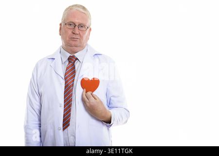 Studio shot of sad mature man doctor holding red heart against chest Stock Photo