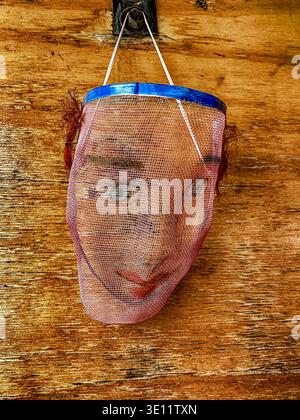 A wire mask hanging from a hook on a wall is used in theatrical performances as a white face mask to change the complexion of actors with dark skins. Stock Photo