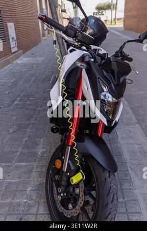 Barcelona, Spain - March 14, 2026: White motorcycle parked on a city sidewalk secured with a yellow anti-theft disc lock, useful for urban transport a Stock Photo