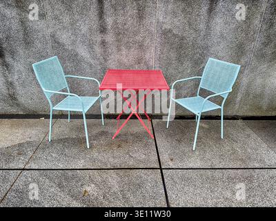 Outdoor furniture with a red table and blue chairs provide color to a concrete courtyard that would otherwise be bland. Stock Photo