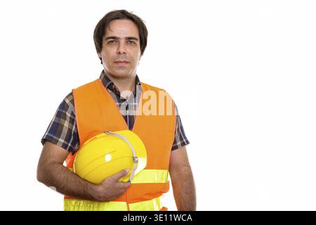 Studio shot of young Persian man construction worker holding safety helmet Stock Photo