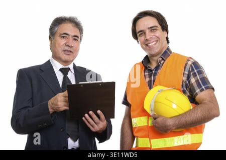 Happy senior Persian businessman holding clipboard with young Persian man construction worker smiling Stock Photo