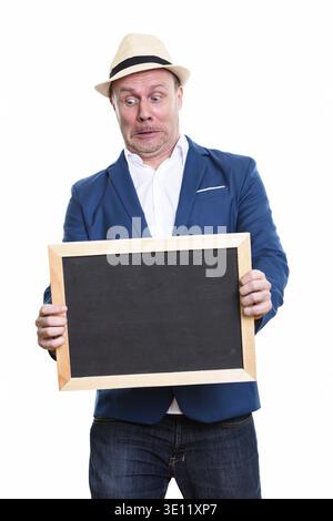 Mature businessman holding blank blackboard while looking shocked and surprised Stock Photo