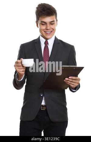 Young happy businessman smiling while reading on clipboard and holding coffee cup Stock Photo