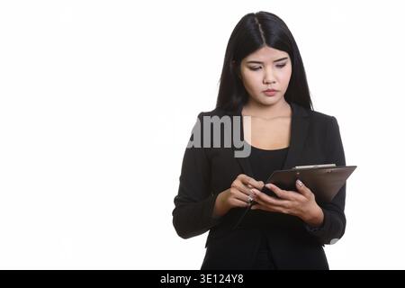 Studio shot of young Asian businesswoman reading on clipboard Stock Photo