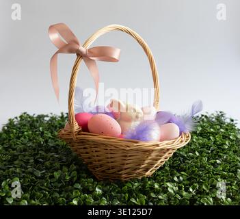 Easter basket with eggs, rabbit and feathers on a white background. Beautiful Easter composition with a basket on a green lawn. Stock Photo