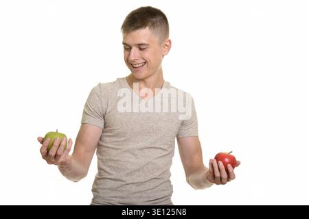 Young happy Caucasian man smiling while choosing between red and green apple Stock Photo