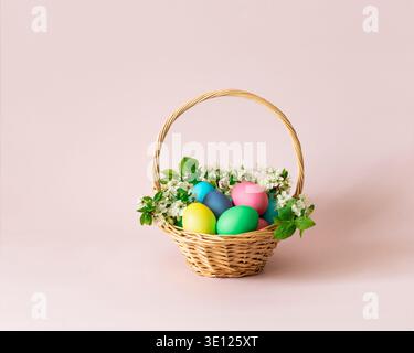 Easter painted eggs in a basket with flowers on a pink background. Easter cute greeting card. Space for text. Stock Photo