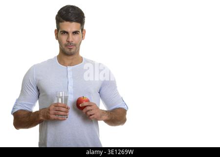 Young handsome Persian man holding glass of water and red apple isolated against white background Stock Photo