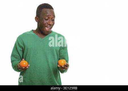 Young happy African man smiling and looking surprised while holding two oranges Stock Photo