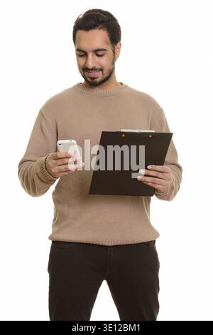 Young happy Indian man holding clipboard while using mobile phone Stock Photo
