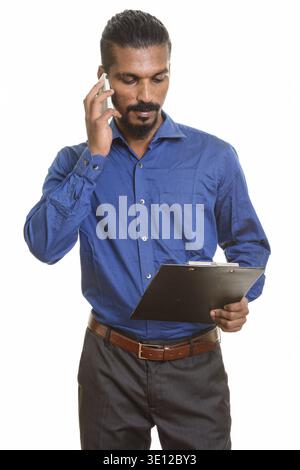 Young Indian businessman talking on mobile phone while holding clipboard Stock Photo