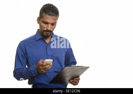 Young Indian businessman using mobile phone while holding clipboard Stock Photo