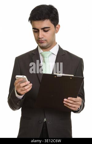 Young handsome Persian businessman holding clipboard while using mobile phone Stock Photo