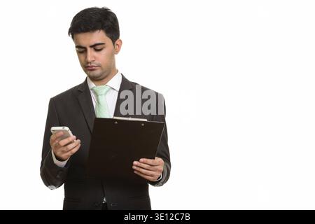 Young handsome Persian businessman holding clipboard while using mobile phone Stock Photo