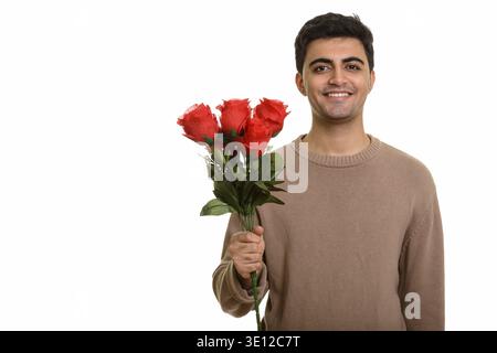 Young happy Persian man holding red roses ready for Valentine's day Stock Photo