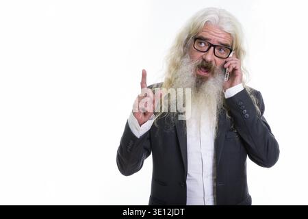 Studio shot of senior bearded businessman talking on mobile phone Stock Photo