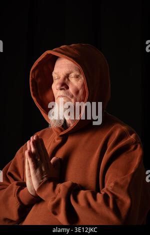 man, praying with closed eyes and foldet hands, black background indoor Stock Photo
