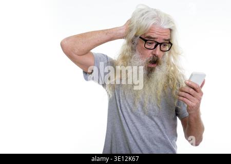 Studio shot of senior bearded man using mobile phone while looking confused Stock Photo