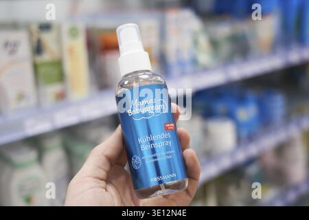 Cooling leg spray from Mama's Babydream in hand. In the background, blurred shelves of a drugstore, in the Rossmann drugstore Stock Photo