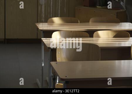 An inviting classroom scene with desks and chairs, bathed in warm sunlight streaming through blinds Stock Photo