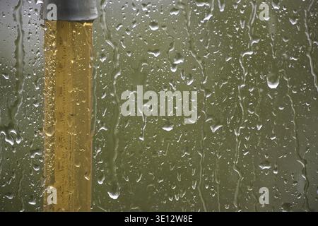 Close-up shot of raindrops on a glass pane, alongside a yellow pole, creating a serene and tranquil atmosphere Stock Photo