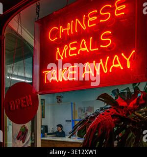 Neon Chinese Takeaway Sign Glowing at Night with Owner alone waiting for customers. Night photo. Urban street Photography.  Bridport, Dorset. Food. Stock Photo