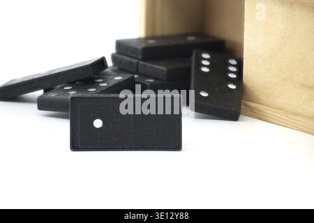 Wooden box with black domino tiles, the box's lid is slightly open and several tiles scattered outside Stock Photo