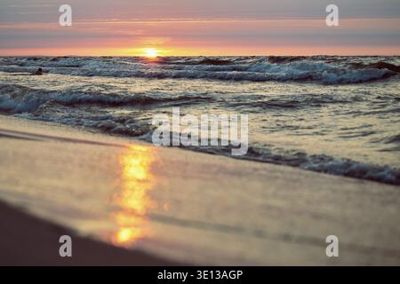 Sunset or sunrise over the sea waves on beach. Sunlight reflections. Dramatic scene. Summer mood. Magic subtle sunlight. Soft colors. Small clouds in Stock Photo