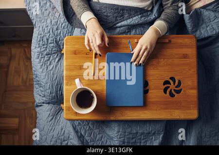 Young woman opening diary, writing journal. Making notes in diary sitting in bed at home Stock Photo