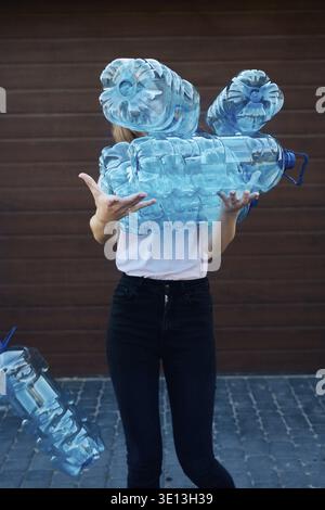 Young woman throwing out empty used plastic water bottles into trash bin. Collecting plastic waste to recycling. Concept of plastic pollution and too Stock Photo
