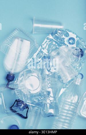 Squashed empty plastic bottles, cups, packagings, market bags and caps over blue background. Collecting plastic waste to recycling. Concept of plastic Stock Photo