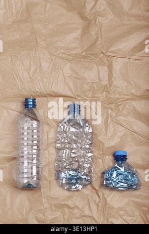 Squashed empty plastic bottles put in a row, over crumpled brown paper background. Collecting plastic waste to recycling. Concept of plastic pollution Stock Photo