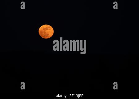 Large orange full moon in the upper left third of the frame against a dark night sky Stock Photo
